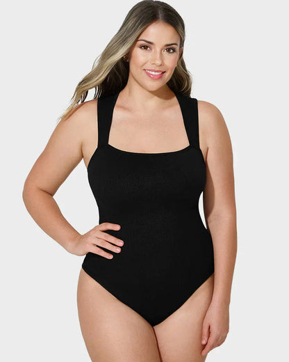Woman wearing black shapewear bodysuit with wide straps, posing against light background