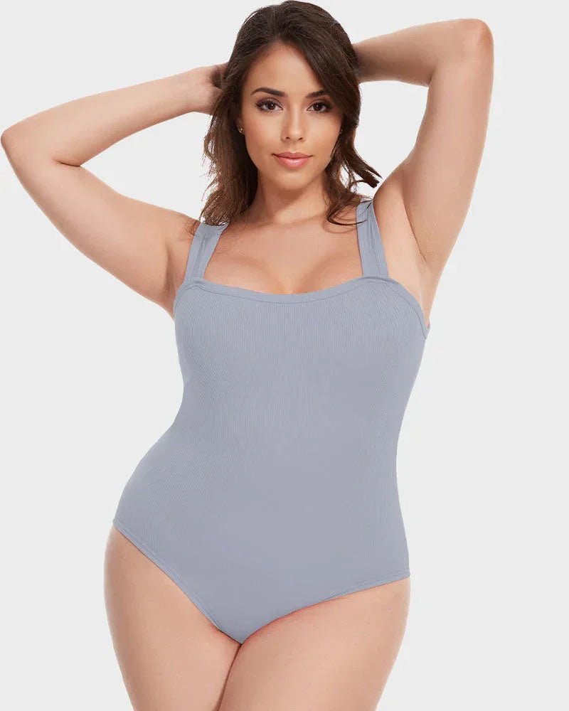 Woman wearing light gray shaping bodysuit with wide straps, posing against a white background